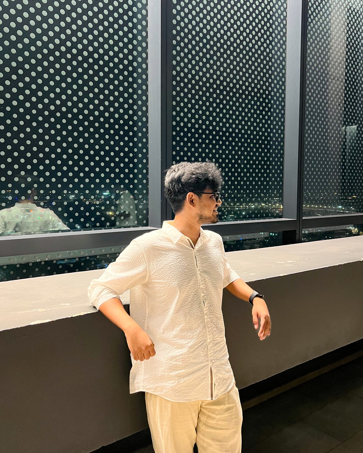 Rishad Rahman in a white shirt, leaning on a rooftop ledge with the city lights behind